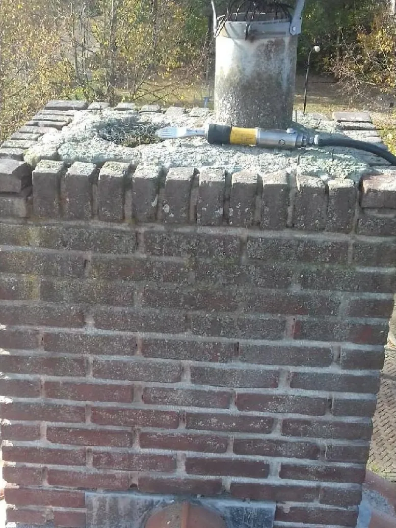 Schoorsteen voor de reparatie, met verweerd metselwerk en oude kap